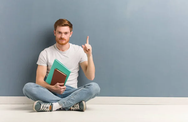 Jovem Estudante Ruivo Sentado Chão Mostrando Número Ele Tem Livros — Fotografia de Stock