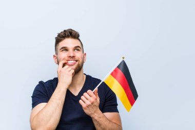 Almanya bayrağı taşıyan genç beyaz adam bir kopya alanına bakan bir şey hakkında düşünerek rahatladı.