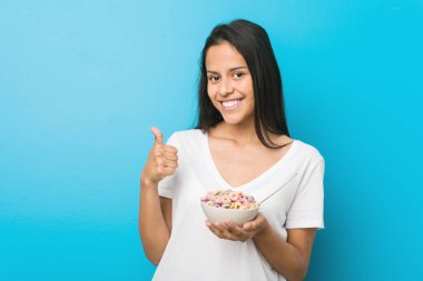 Genç İspanyol kadın gülümseyerek bir şeker tahıl kase tutan ve başparmak yükselterek
