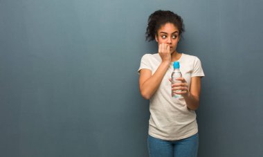 Tırnaklarını ısıran genç siyah kadın, sinirli ve çok endişeli. Elinde bir su şişesi var..