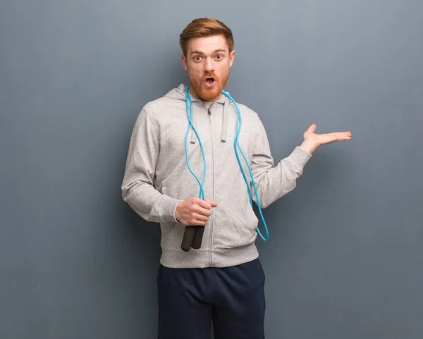 Young redhead fitness man holding something on palm hand. He is holding a jump rope.