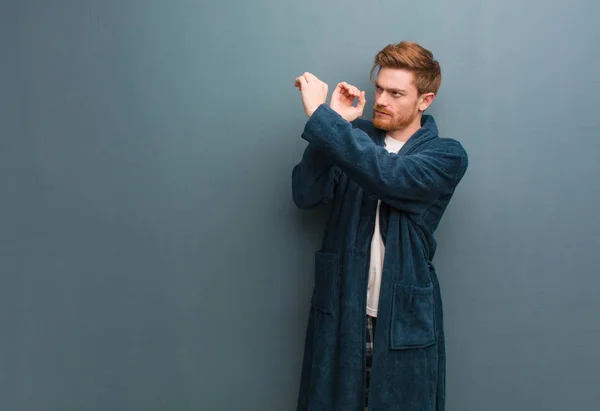 Young redhead man in pajama making the gesture of a spyglass