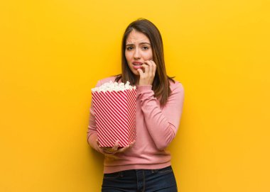 Genç sevimli kadın çivi ısırma bir patlamış mısır kova tutan, sinir ve çok endişeli