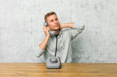Genç adam başının arkasına dokunarak, düşünme ve bir seçim yapma bir vintage telefon konuşuyor.