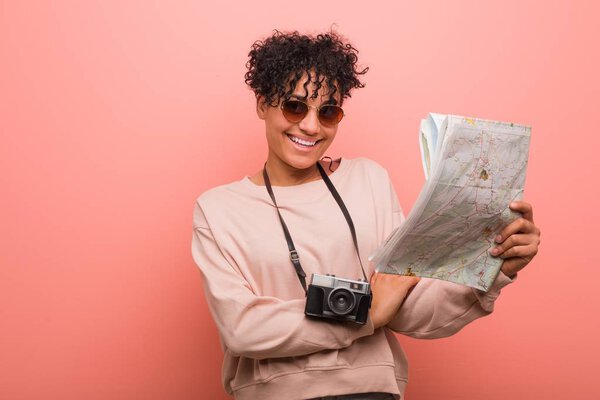 Young african american woman holding a map smiling confident with crossed arms.