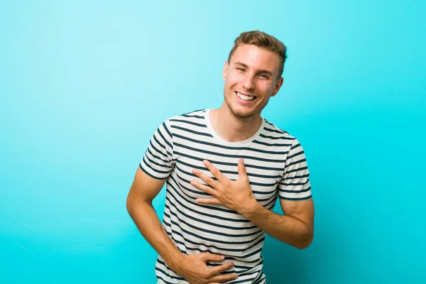 青い壁に対する若い白人男性は楽しく笑い 胃の上に手を保つ楽しみを持っています — ストック写真