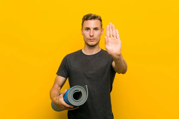 Młody Kaukaski Mężczyzna Trzyma Mat Stojący Wyciągniętą Ręką Pokazując Znak — Zdjęcie stockowe