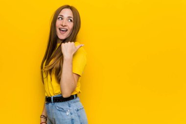 Young ginger redhead woman points with thumb finger away, laughing and carefree.