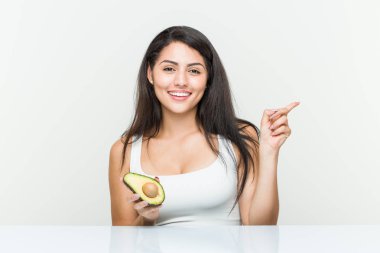 Avokado tutan genç İspanyol kadın işaret parmağıyla işaret ederek gülümsüyor..