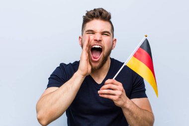 Young caucasian man holding a germany flag shouting excited to front.