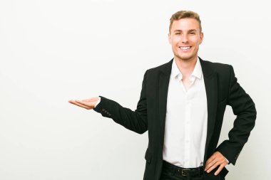 Young caucasian business man showing a copy space on a palm and holding another hand on waist.