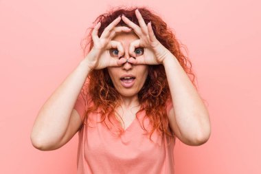 Young natural and authentic redhead woman showing okay sign over eyes