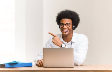 Young telemarketer black man smiling and pointing to the side