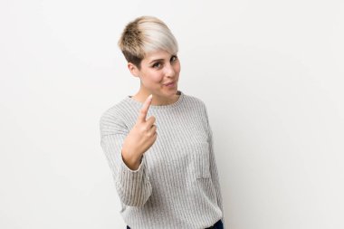Young curvy caucasian woman isolated on white background pointing with finger at you as if inviting come closer.
