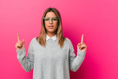 Bir duvara karşı genç otantik karizmatik gerçek insanlar kadın boş bir boşluk gösteren kadar her iki ön parmak ile gösterir.
