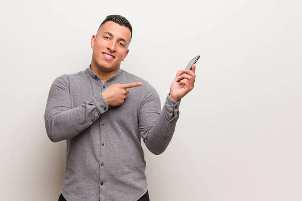 Joven Latino Sosteniendo Teléfono Apuntando Hacia Lado Con Dedo — Foto de Stock