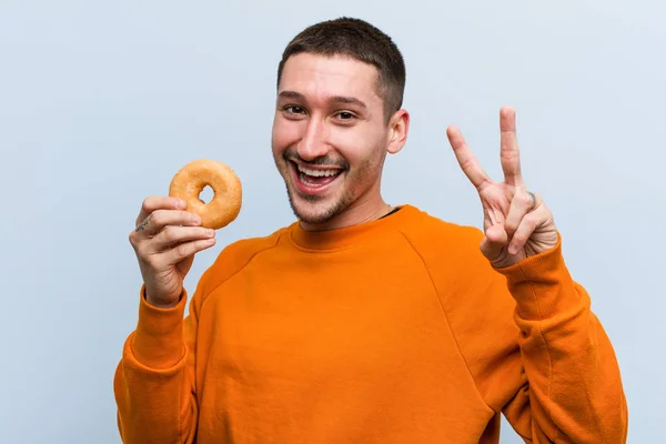 Joven Caucásico Sosteniendo Donut Mostrando Número Dos Con Los Dedos — Foto de Stock