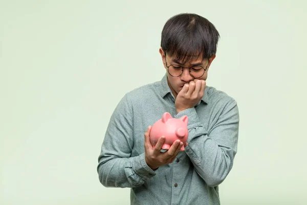Mladý Asijský Muž Drží Prasátko Banky Kousání Nehty Nervózní Velmi — Stock fotografie