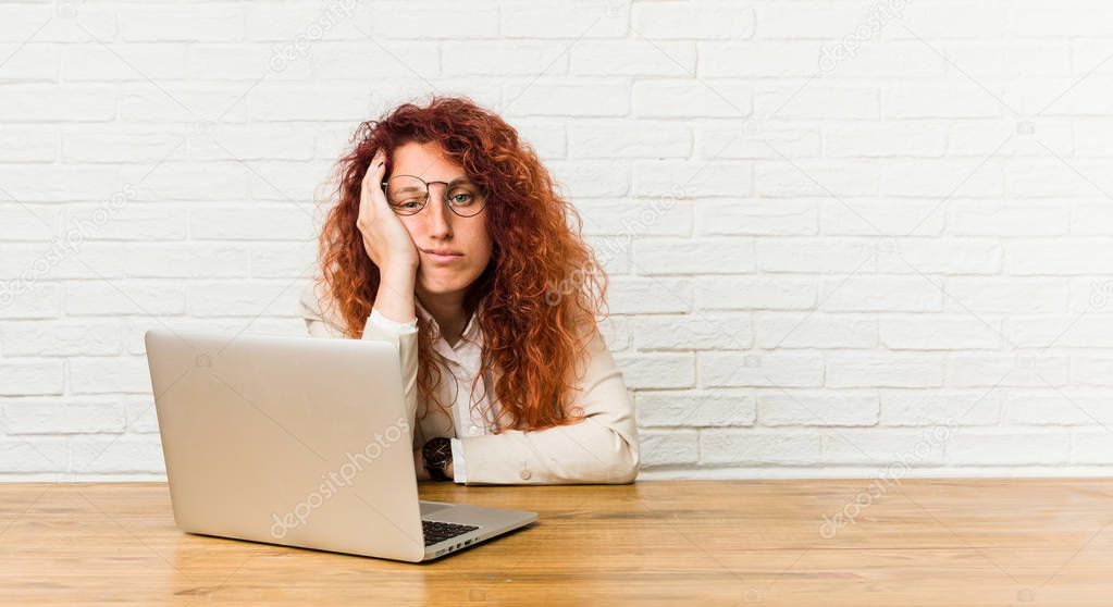Young redhead curly woman working with her laptop who is bored, fatigued and need a relax day.