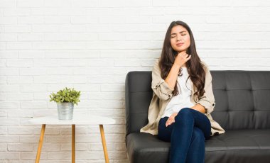 Kanepede oturan genç Arap kadın virüs ya da enfeksiyon yüzünden boğaz ağrısı çekiyor..