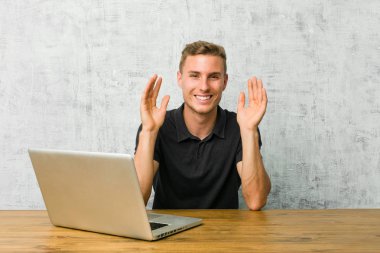 Genç girişimci laptopuyla masasında neşeli bir şekilde gülüyor. Mutluluk kavramı.