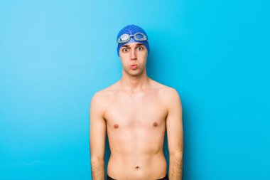 Genç yüzücü yanakları üflüyor, yorgun bir ifadesi var. Yüz ifadesi kavramı.