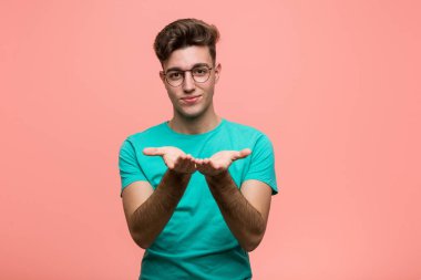 Havalı, beyaz bir adam elinde avuç içi bir şeyle kameraya sunuyor..