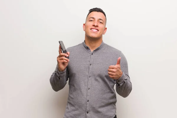 Joven Latino Sosteniendo Teléfono Sonriendo Levantando Pulgar — Foto de Stock