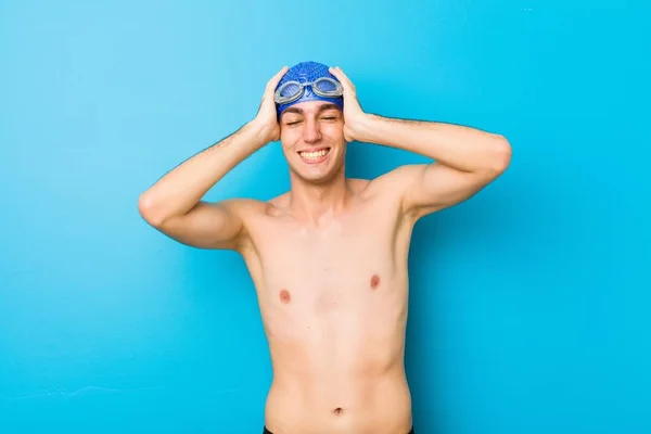 Young swimmer man laughs joyfully keeping hands on head. Happiness concept.