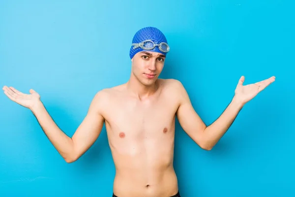 Young swimmer man doubting and shrugging shoulders in questioning gesture.