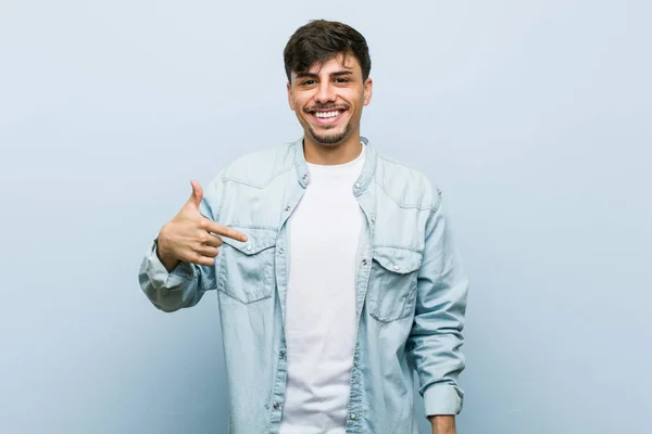 Young hispanic cool man person pointing by hand to a shirt copy space, proud and confident