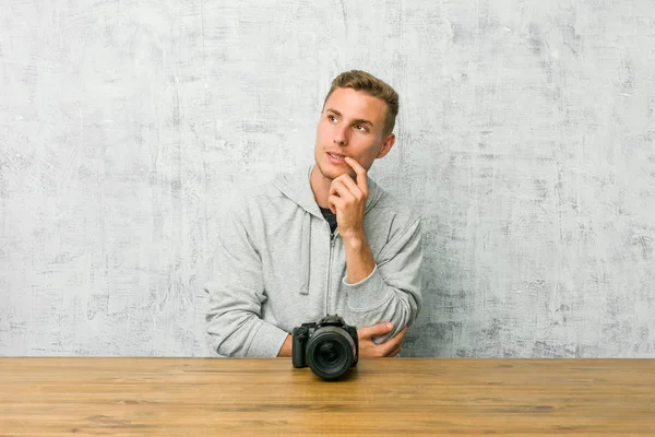 Jovem Fotógrafo Segurando Uma Câmera Uma Mesa Relaxado Pensando Algo — Fotografia de Stock