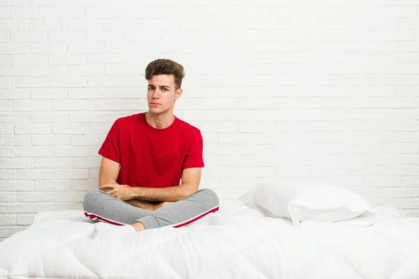 Young teenager student man on the bed unhappy looking in camera with sarcastic expression.