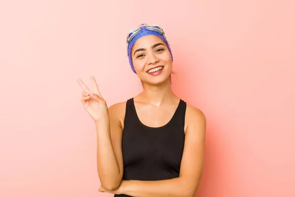 Young arab swimmer woman isolated joyful and carefree showing a peace symbol with fingers.