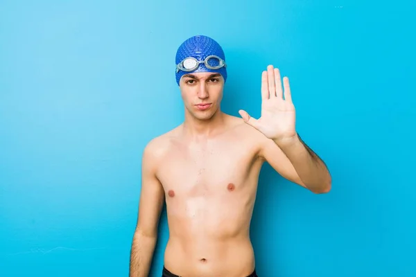 Young swimmer man standing with outstretched hand showing stop sign, preventing you.