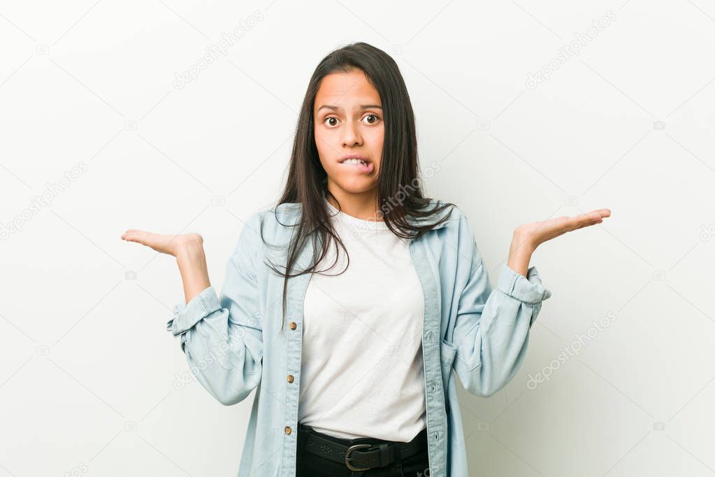 Young hispanic woman confused and doubtful shrugging shoulders to hold a copy space.