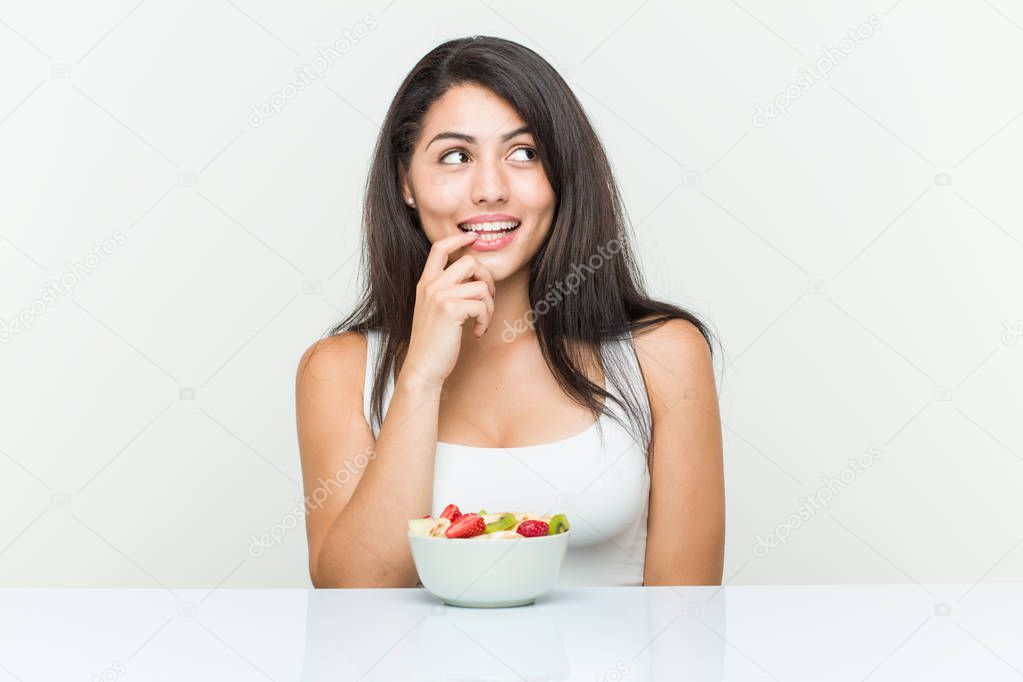 Young hispanic woman eating a fruit bowl relaxed thinking about something looking at a copy space.