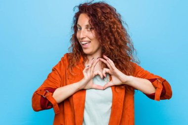 Genç kızıl saçlı zarif kadın gülümsüyor ve elleriyle kalp şeklini gösteriyor..