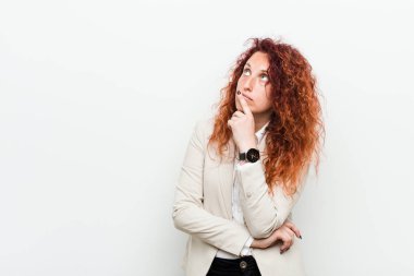 Genç, kızıl saçlı iş kadını, beyaz arka planda izole edilmiş şüpheli ve kuşkulu bir ifadeyle yana bakıyor..