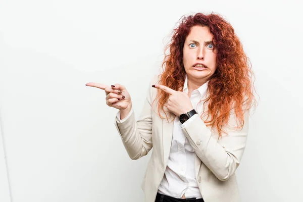 Young natural redhead business woman isolated against white background shocked pointing with index fingers to a copy space.