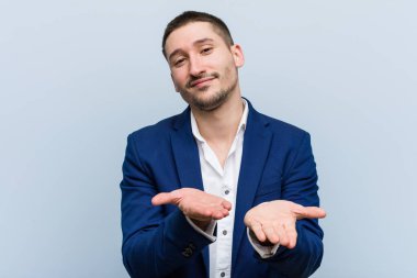 Genç beyaz bir adam elinde avuç içi bir şeyle kameraya sunuyor..