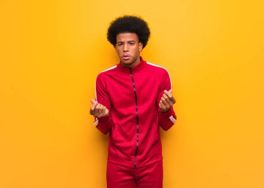 Turuncu bir duvarın üstünde genç bir zenci ihtiyaç jesti yapıyor.