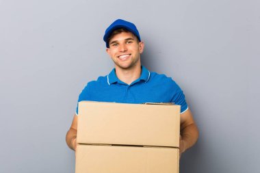 Paketleri teslim eden genç adam mutlu, güler yüzlü ve neşeli.