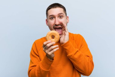 Genç beyaz bir adam elinde donut tutarak heyecanla bağırıyor..