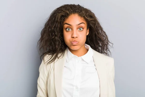 Young african american business woman blows cheeks, has tired expression. Facial expression concept.