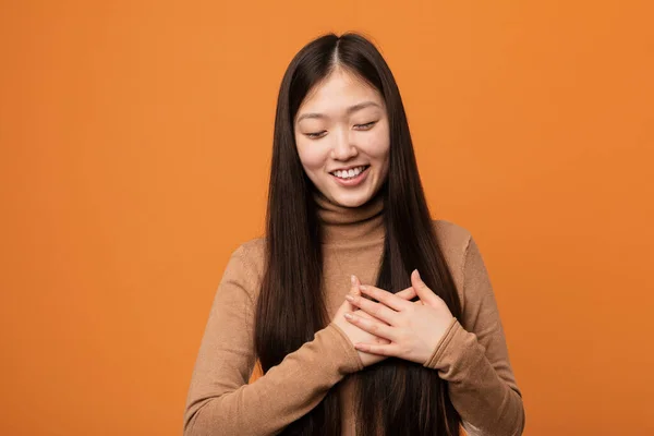 Young pretty chinese woman laughing keeping hands on heart, concept of happiness.