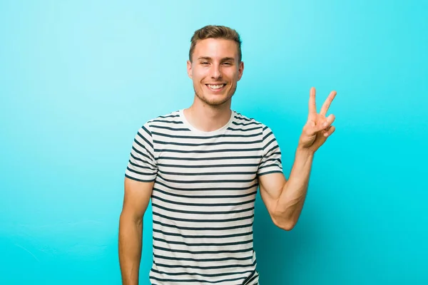 青い壁に対する若い白人男性喜びと屈託のない指で平和のシンボルを示す — ストック写真