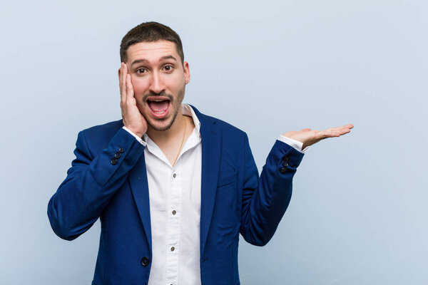 Молодой кавказский бизнесмен держит пространство для копирования на ладони, держит руку за щекой. Удивились и обрадовались
.