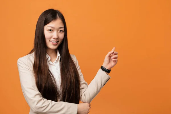 Young business chinese woman smiling cheerfully pointing with forefinger away.