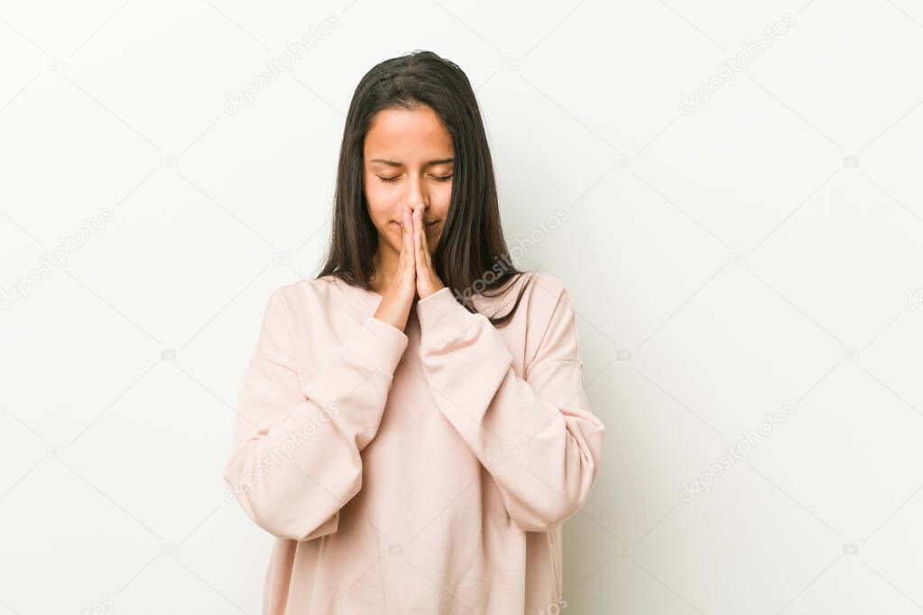 Young cute hispanic teenager woman holding hands in pray near mouth, feels confident.
